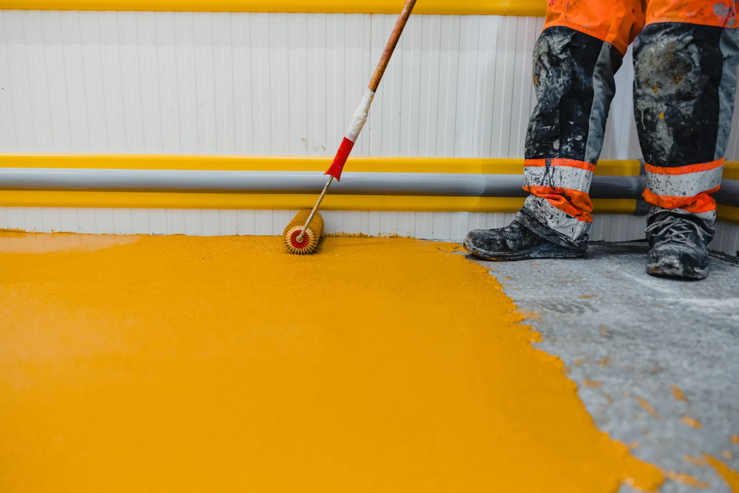A yellow protective floor coating being applied with a roller, illustrative application photography